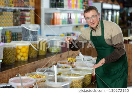 Smiling vendor inviting to buy marinated olives in grocery store Smiling vendor inviting to buy marinated olives in grocery store 139272130