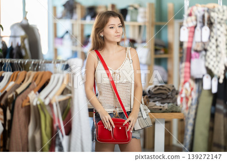 Positive young girl choosing handbag in clothing store 139272147
