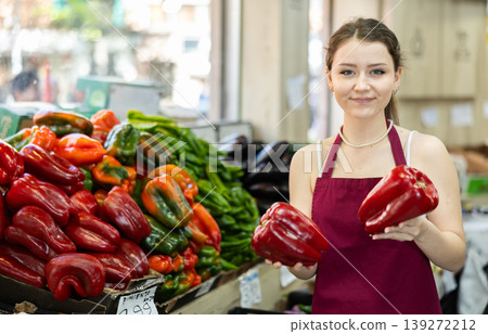 Smiling female saleswoman carefully places ripe bell peppers on a display case at grocery supermarket Smiling female saleswoman carefully places ripe bell peppers on a display case at grocery supermarket 139272212