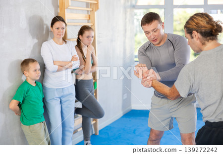 Man coach shows family students technique of performing painful modus with help of wringing hand Man coach shows family students technique of performing painful modus with help of wringing hand 139272242