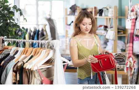 Positive young girl choosing handbag in clothing store Positive young girl choosing handbag in clothing store 139272268