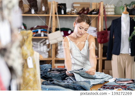 woman stands in a store near a shelf with jeans woman stands in a store near a shelf with jeans 139272269