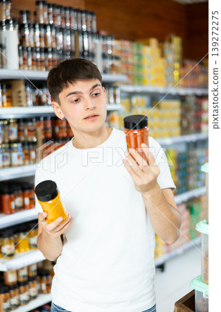 Guy choosing natural aromatic spices in glass jars in grocery store Guy choosing natural aromatic spices in glass jars in grocery store 139272275