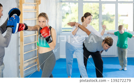 Teen girl in boxing gloves practices punches with trainer in mitts in sport club during family training Teen girl in boxing gloves practices punches with trainer in mitts in sport club during family training 139272279