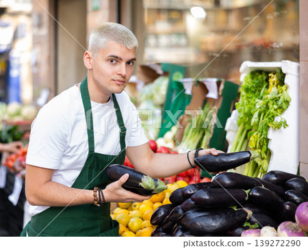 Young guy seller puts eggplants in vegetable shop Young guy seller puts eggplants in vegetable shop 139272290