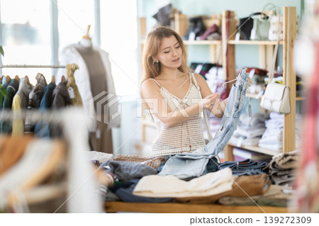 Positive young girl choosing jeans pantaloons in clothing store Positive young girl choosing jeans pantaloons in clothing store 139272309