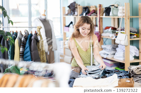 Positive young girl choosing jeans pantaloons in clothing store Positive young girl choosing jeans pantaloons in clothing store 139272322