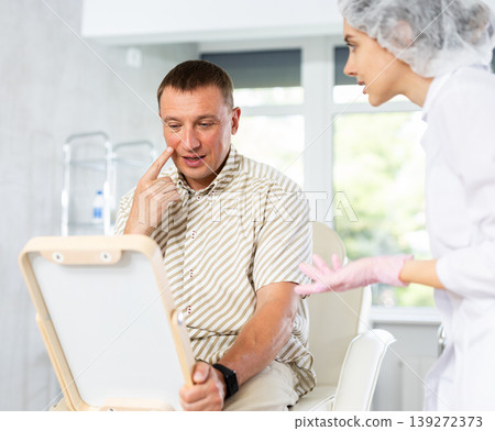 Man looks in mirror and rejoices at successful treatment of dermatological problems of face Man looks in mirror and rejoices at successful treatment of dermatological problems of face 139272373