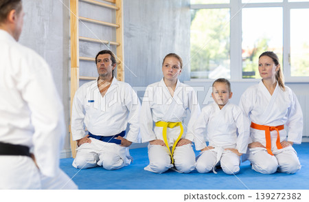 Family in gym at group karate training with trainer are in sitting position Family in gym at group karate training with trainer are in sitting position 139272382