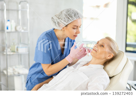Professional cosmetologist performing lip filler injections to senior woman Professional cosmetologist performing lip filler injections to senior woman 139272403