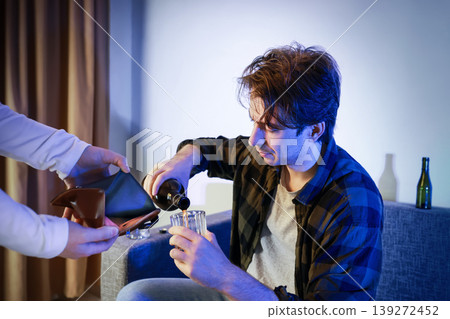 Alcoholism and unemployment concept: a disheveled man pours a drink as he is shown an empty wallet. Themes of addiction, drunkenness, separation, and divorce. Alcoholism and unemployment concept: a disheveled man pours a drink as he is shown an empty wallet. Themes of addiction, drunkenness, separation, and divorce. 139272452
