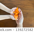An adult and a child holding orange origami cranes together 139272582