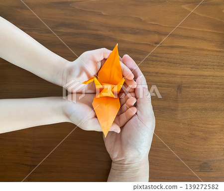An adult and a child holding orange origami cranes together An adult and a child holding orange origami cranes together 139272582