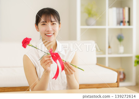 Mother's Day: A young Japanese girl gives carnations in her living room at home. Mother's Day: A young Japanese girl gives carnations in her living room at home. 139272614
