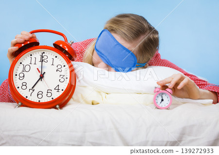 Sleeping woman wearing pajamas holding clock Sleeping woman wearing pajamas holding clock 139272933