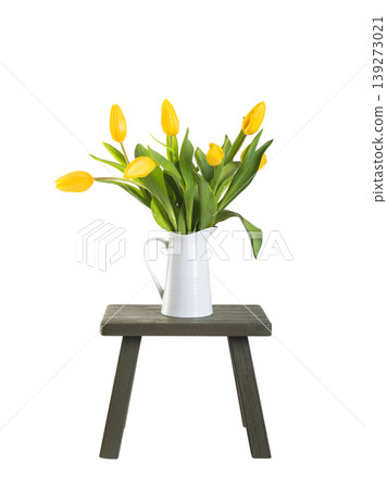 A colourful blooming bouquet of tulips in a white vase on an old wooden stool infront of a plain white background 139273021