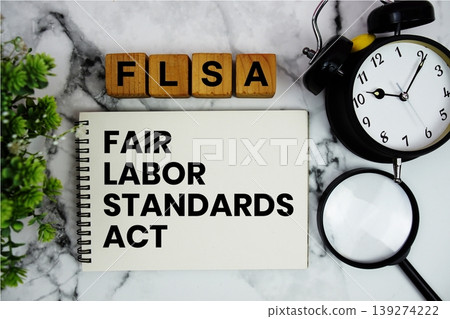 FLSA Fair Labor Standards Act text with alarm clock and magnifying glass on marble background FLSA Fair Labor Standards Act text with alarm clock and magnifying glass on marble background 139274222