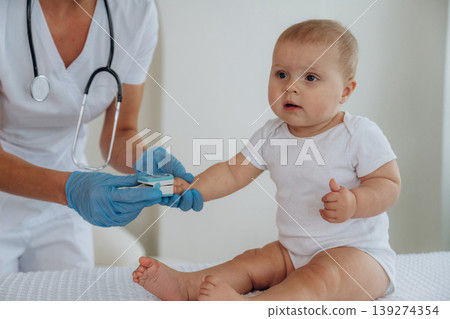 The oxygen in blood meter tool. Female doctor is taking care of little baby girl in the clinic The oxygen in blood meter tool. Female doctor is taking care of little baby girl in the clinic 139274354