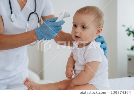 Temperature of body measurement. Female doctor is taking care of little baby girl in the clinic Temperature of body measurement. Female doctor is taking care of little baby girl in the clinic 139274364