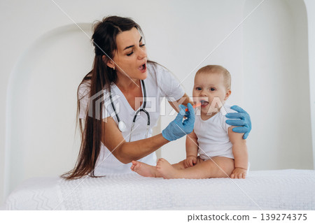 Giving medicine in syringe. Female doctor is taking care of little baby girl in the clinic 139274375