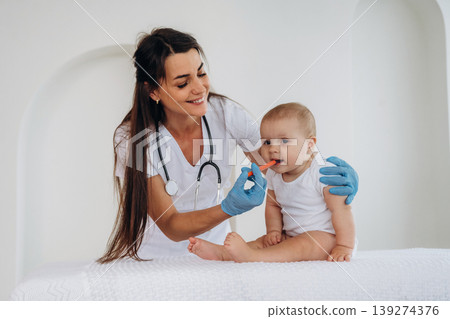 Giving medicine in syringe. Female doctor is taking care of little baby girl in the clinic Giving medicine in syringe. Female doctor is taking care of little baby girl in the clinic 139274376