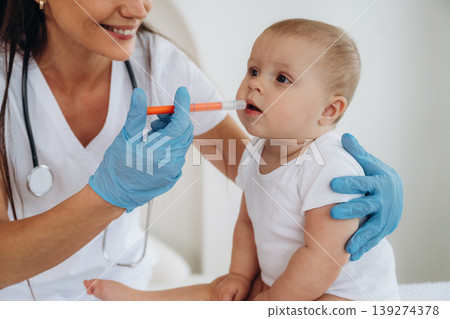Giving medicine in syringe. Female doctor is taking care of little baby girl in the clinic Giving medicine in syringe. Female doctor is taking care of little baby girl in the clinic 139274378