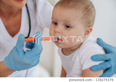 Giving medicine in syringe. Female doctor is taking care of little baby girl in the clinic Giving medicine in syringe. Female doctor is taking care of little baby girl in the clinic 139274379