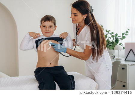 Listening to the breathing, using stethoscope. Boy is in routine appointment in clinic with female doctor 139274416