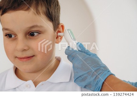 Ear temperature measurement. Boy is in routine appointment in clinic with female doctor Ear temperature measurement. Boy is in routine appointment in clinic with female doctor 139274424