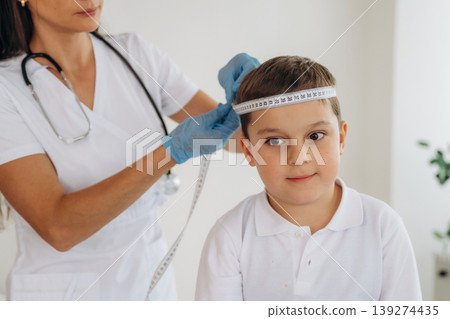 Measuring the width of head. Boy is in routine appointment in clinic with female doctor Measuring the width of head. Boy is in routine appointment in clinic with female doctor 139274435
