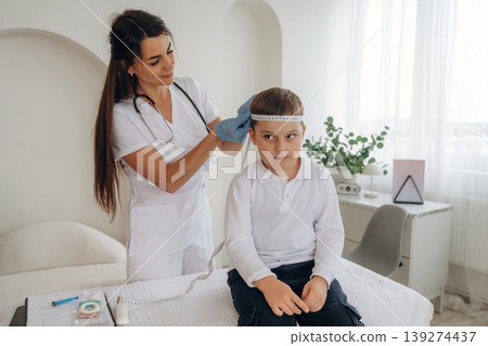 Measuring the width of head. Boy is in routine appointment in clinic with female doctor Measuring the width of head. Boy is in routine appointment in clinic with female doctor 139274437