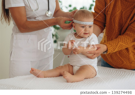 Head width measurement. Mother with her little baby daughter is in clinic with doctor at appointment Head width measurement. Mother with her little baby daughter is in clinic with doctor at appointment 139274498