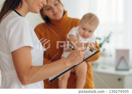 Using pen, writing information. Mother with her little baby daughter is in clinic with doctor at appointment 139274505