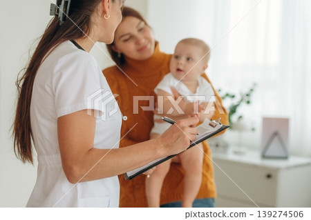 Using pen, writing information. Mother with her little baby daughter is in clinic with doctor at appointment 139274506