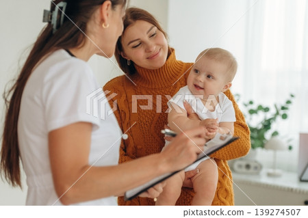 Using pen, writing information. Mother with her little baby daughter is in clinic with doctor at appointment Using pen, writing information. Mother with her little baby daughter is in clinic with doctor at appointment 139274507