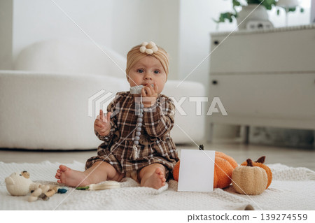 Cute little baby is sitting on the floor at home with pumpkins toys 139274559