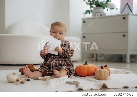 Copy space paper is in hands. Cute little baby is sitting on the floor at home with pumpkins toys 139274562