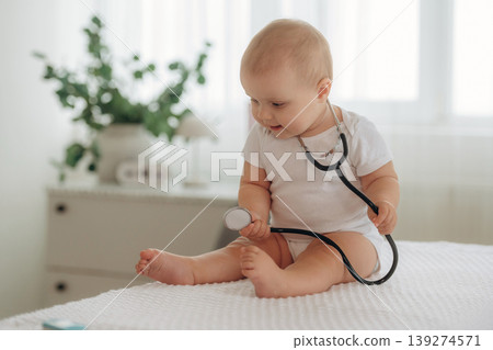 The stethoscope is on the neck. Playful happy little baby is at home in domestic room The stethoscope is on the neck. Playful happy little baby is at home in domestic room 139274571