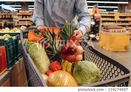 Cabbage, tomatoes, bananas in the shopping cart. Close up view of man that is in the grocery store Cabbage, tomatoes, bananas in the shopping cart. Close up view of man that is in the grocery store 139274987