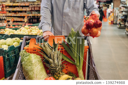 Cabbage, tomatoes, bananas in the shopping cart. Close up view of man that is in the grocery store Cabbage, tomatoes, bananas in the shopping cart. Close up view of man that is in the grocery store 139274988