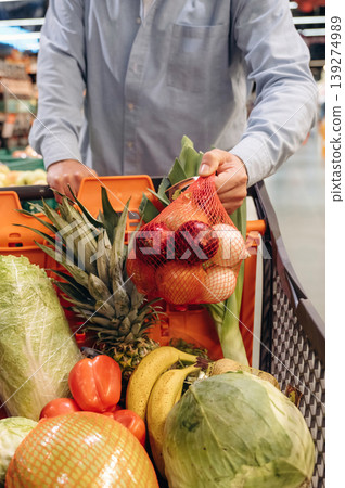 Cabbage, tomatoes, bananas in the shopping cart. Close up view of man that is in the grocery store Cabbage, tomatoes, bananas in the shopping cart. Close up view of man that is in the grocery store 139274989