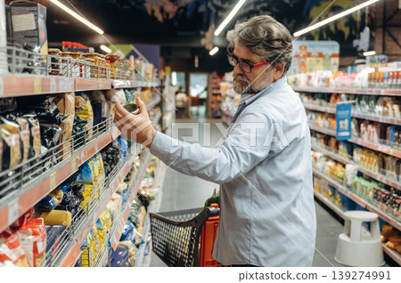 Taking the products from the shelves. A senior man is buying food in the grocery store Taking the products from the shelves. A senior man is buying food in the grocery store 139274991