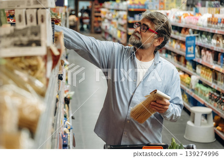 Taking the products from the shelves. A senior man is buying food in the grocery store Taking the products from the shelves. A senior man is buying food in the grocery store 139274996