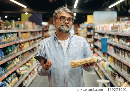 Smartphone is in hand. A senior man is buying food in the grocery store Smartphone is in hand. A senior man is buying food in the grocery store 139275001