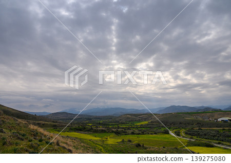 Rolling green hills stretch under a cloudy sky with distant mountains Rolling green hills stretch under a cloudy sky with distant mountains 139275080