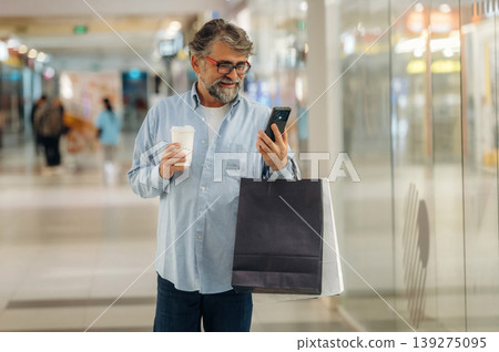 Cup of drink and smartphone are in hands. Senior man is in the mall, shopping time conception 139275095