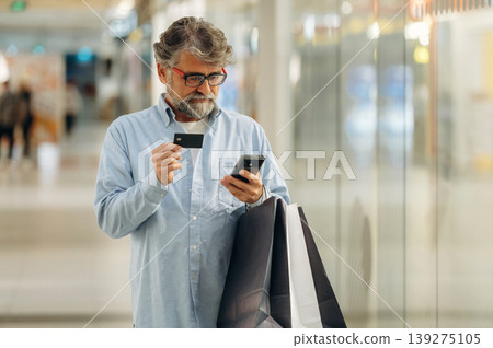 Debit or credit card and smartphone are in hands. Senior man is in the mall, shopping time conception 139275105