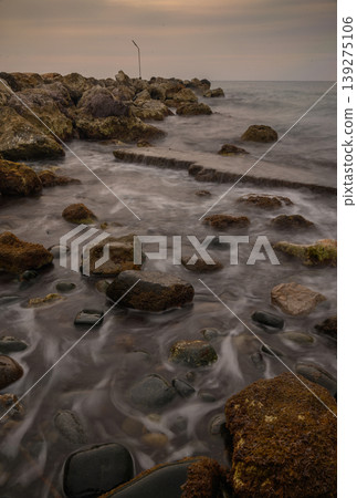 Calm waves embrace the rocky shore at twilight along a serene coastline 139275106