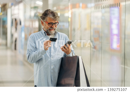 Debit or credit card and smartphone are in hands. Senior man is in the mall, shopping time conception 139275107