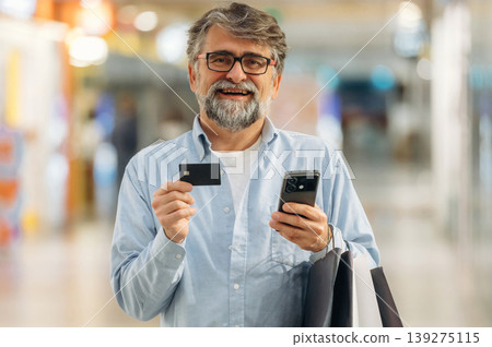 Wireless payment by using credit card and smartphone. Senior man is in the mall, shopping time conception Wireless payment by using credit card and smartphone. Senior man is in the mall, shopping time conception 139275115